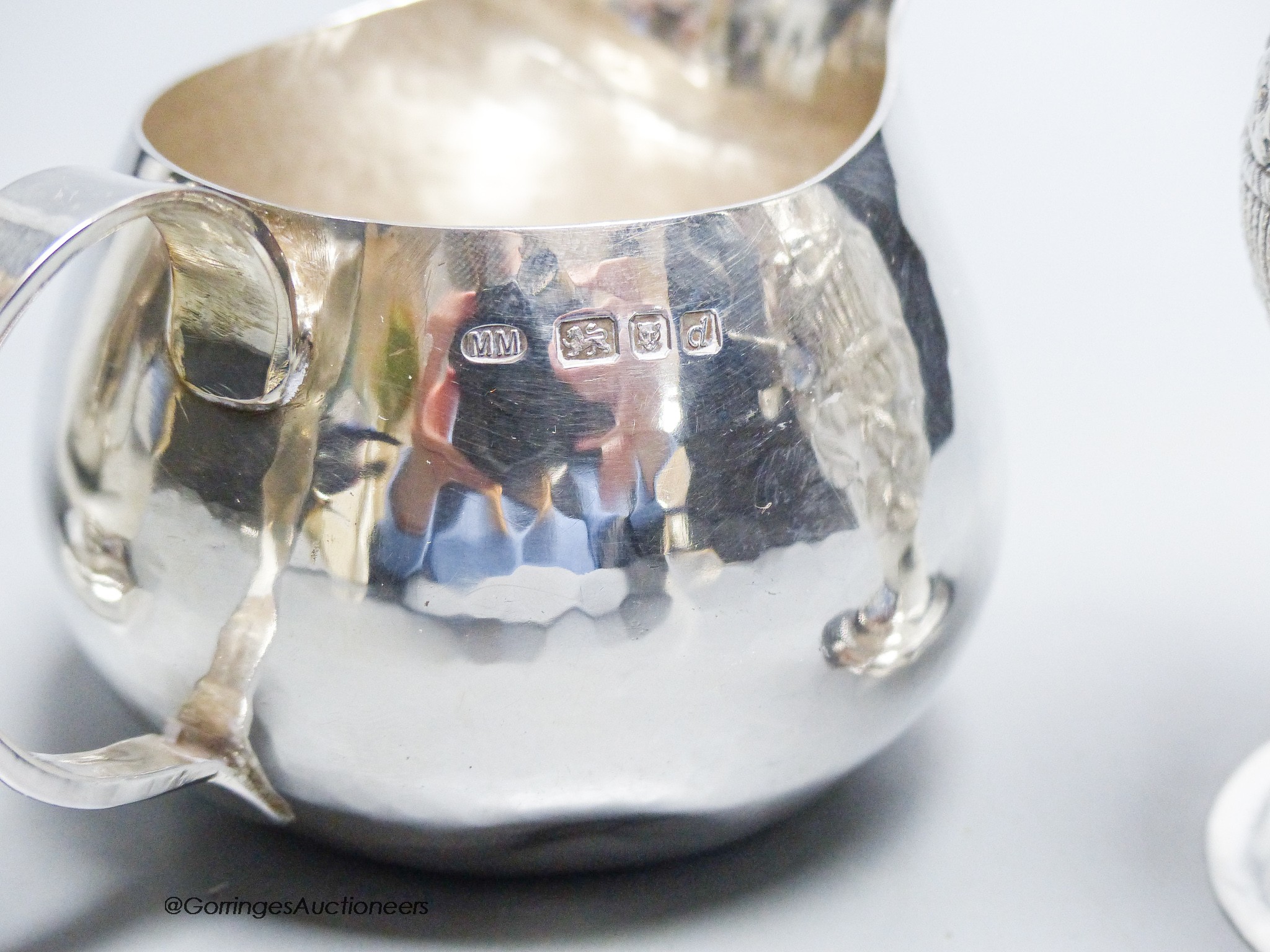 A George III later embossed silver cream jug with later base?, 11.5cm, a modern silver cream jug and a French white metal beaker, gross 10.5oz.